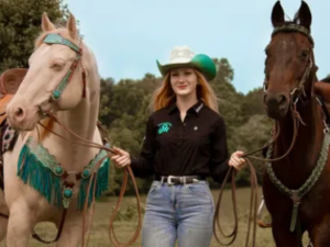 Western Team Coach Julz Williams stands between two horses, one cremello and one bay, holding their reins.